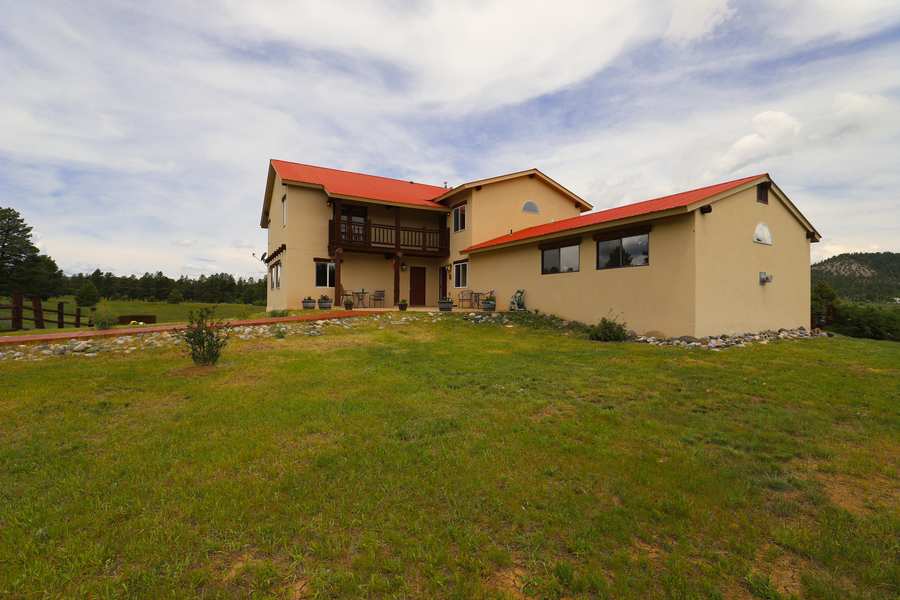 Piedra Pines Lodge, a Santa Fe style lodge with a red metal roof, seen from behind the split-rail fence